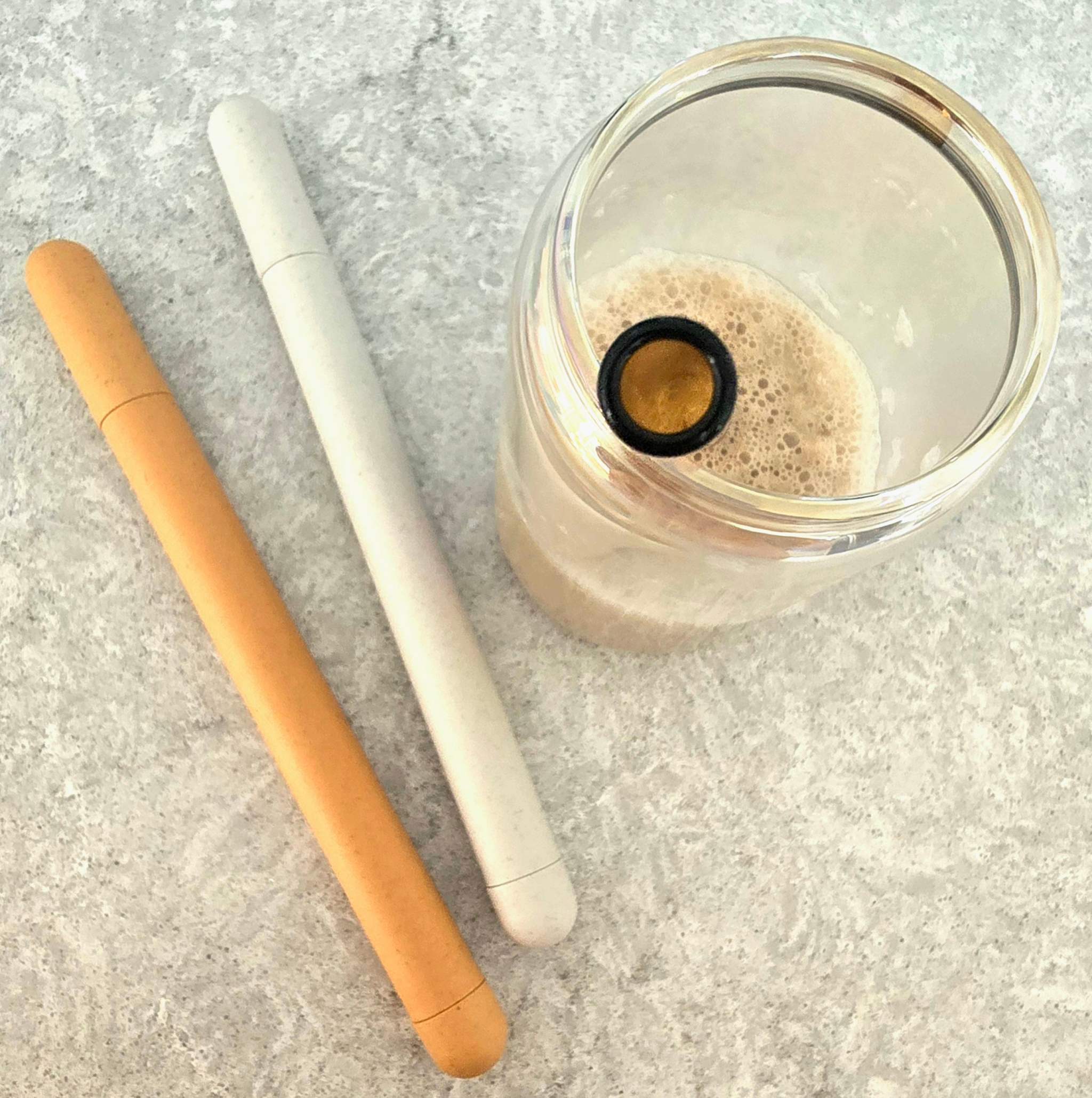 Two reusable glass straws in Sunset Bliss and Desert Bloom colors, displayed with a compact carrying case on a wooden surface.